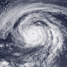A satellite image of a well-organized hurricane with a tightly-wound circulation, spiral bands fanning out, and a clear eye; an arc of thin, high clouds is to the north and northwest of the hurricane