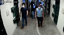 A screenshot of video surveillance footage showing various men waring face masks inside a prison hallway