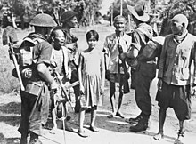 Black and white photo of three men wearing military uniforms and carrying guns with three elderly men and a teenager wearing civilian clothes