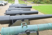Photo shows a row of 1860s cannon barrels. The one in the foreground has twin handles attached to the barrel.