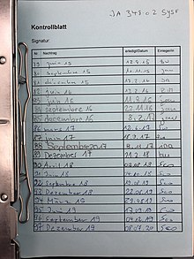 Photographie d'une feuille bleue dans un classeur, intitulée Kontrollblatt pourvue d'un tableau ayant des dates allant de juin 2015 à décembre 2019