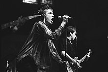Members of rock band the Sex Pistols onstage in a concert. From left to right, singer Johnny Rotten and electric guitarist Steve Jones.