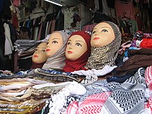 Four mannequin heads with different headscarfs are arranged on top of a display-table of colourful headscarfs.