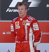 Kimi Räikkönen dons red fireproof overalls as he stands on a podium with a bottle of champagne