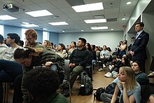 Lee Roberts stands to the right in a crowded room during a teach in