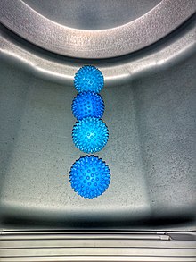 Four spike-covered blue rubberized dryer balls sit in a line in the bottom of the metal drum inside a clothes dryer.