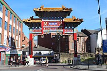A red gold and blue Chinese arch over a busy city centre street