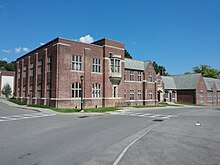 A two-story brick building extends from the foreground off to the right side of the frame. A road runs before it. The day is sunny and clear.