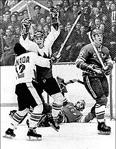 man wearing jersey and hockey equipment on skates with both hands raised high