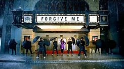 A faraway image of Lewis and multiple men. She wears a raincoat and leggings. The men wear black clothes and all carry an umbrella. They are in front of a theatre. On the marquee, it is written "Forgive Me" in capital letters. Also, it is raining.