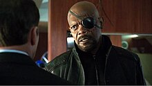 Man with an eye patch over his left eye talking to another man, in an over the shoulder shot