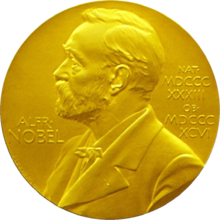 A golden medallion with an embossed image of Alfred Nobel facing left in profile. To the left of the man is the text "ALFR•" then "NOBEL", and on the right, the text (smaller) "NAT•" then "MDCCCXXXIII" above, followed by (smaller) "OB•" then "MDCCCXCVI" below.