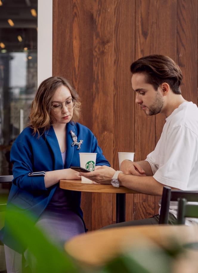 Мужчина и женщина сидят в кафе и смотрят в телефон