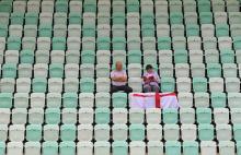 Two England supporters sit in a the near empty stadium waiting for the start of the preliminary round group B netball match between England and Barbados at the Thyagaraj Sports Complex