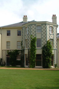 A large, cream-coloured house with trellises stands beyond a mown lawn.