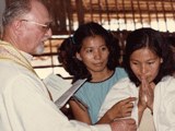 Father Robert Venet performing a baptism for Cambodian refugees, 1986