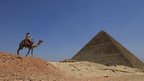 A man rides a camel past a pyramid at Giza
