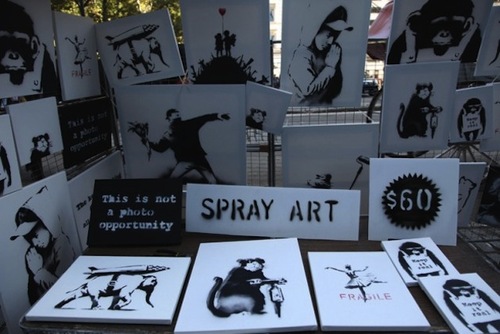 Banksy In Central Park
The elusive street artist Banksy set up shop in Central Park over the weekend, selling original artwork for $60 each, with an elderly man working the pop-up stall at the edge of the park on Fifth Ave. Most people strolled by without taking a second look and, according to Banksy, it took about 4 hours for the first sale to be made, but only after a 50% discount was negotiated.
Considering that his work has been auctioned worldwide for hundreds of thousands of dollars in the past, this latest move by the artist is unexpected and quite ironic. 