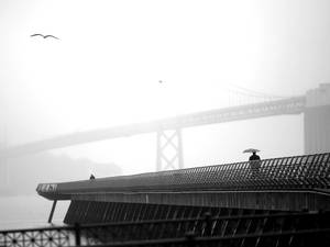 7 February 2014: A man walks beneath an umbrella along Pier 14 near the San Francisco Oakland Bay Bridge during a light rain in San Francisco