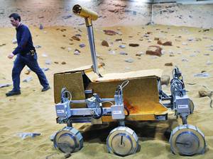 28 March 2014: Engineer Ben Nye walks past a robotic vehicle on the 'Mars Yard Test Area', a testing ground for the robotic vehicles of the European Space Agency's ExoMars program scheduled for 2018, in Stevenage
