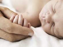 A mother holds the hand of her sleeping newborn son