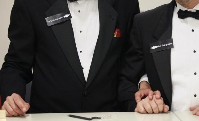 Two men, both wearing signs that read ''he's the groom'', hold hands shortly after midnight after getting a civil union when Colorado's civil union law went into effect in Denver May 1, 2013.  REUTERS/Rick Wilking