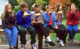Comment: A group of children sit on a bench eating slices of pizza