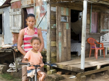 mother, daughter, family, Nicaraguan, Nicaragua, bicycle, poverty, house, ramshackle, shack, hut, clapboard, jungle, coconut tree, palm tree, girl, woman, young, native, black, African, Latin, Latina, Hispanic, Spanish, Central America, home, residence, happy, smiling, smile, riding, ride, transport, transportation, music player, machine, music machine, head-phone, listen, listening, nature