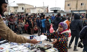 Photo purportedly shows Islamic State militant (left) distributing soft drinks, sweets and biscuits along with religious pamphlets to a young girl in Raqqa in January.