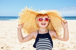 Smiling girl in swimsuit and straw hat on white beach