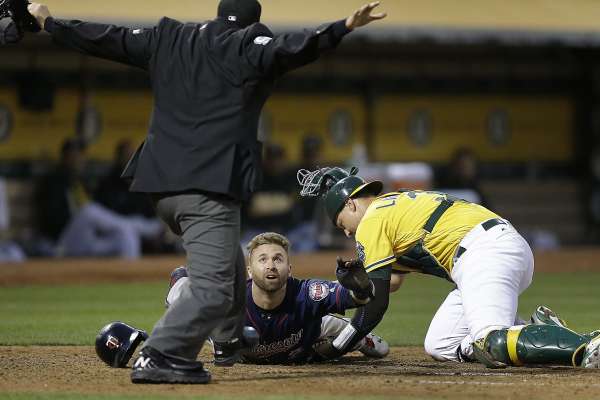 Minnesota Twins' Brian Dozier looks to home plate umpire Mark Ripperger for the call as he scores past Oakland Athletics catcher Ryan Lavarnway, right, during the fourth inning of a baseball game Friday, July 28, 2017, in Oakland, Calif. (AP Photo/Ben Margot)