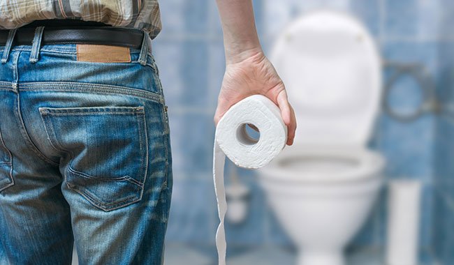 Image of a man walking towards a toilet with a roll of toilet paper in hand