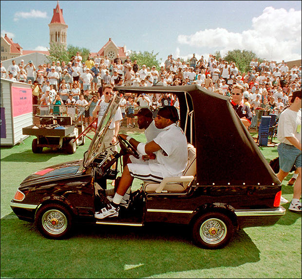 Then-Dallas Cowboy Deion Sanders takes a ride in a custom golf cart in front of St. Edward's main building. 