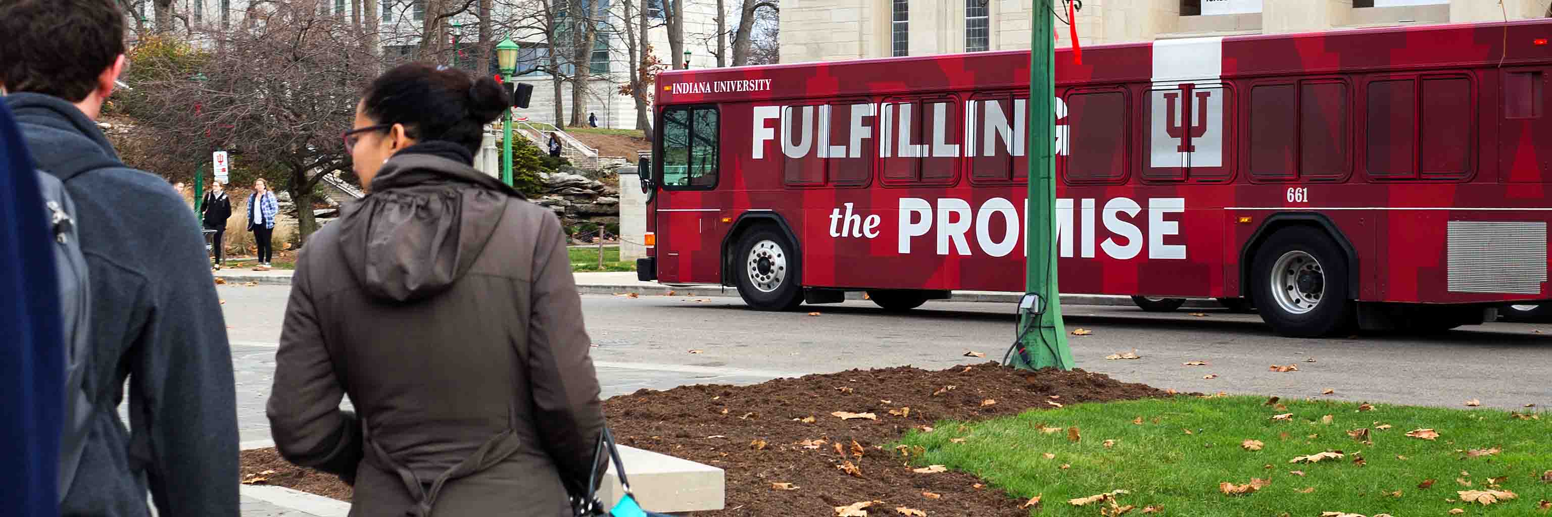 two students walking towards an IU "fulfilling the promise" bus.