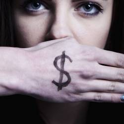 A woman's face with a hand covering her mouth, dollar sign written on the hand.