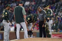 Oakland Athletics shortstop Marcus Semien, left, manager Bob Melvin, a member of the staff, second from right, and catcher Jonathan Lucroy (21) all check on relief pitcher Blake Treinen, center, after Treinen was hit in the lower legs by a line drive back to the mound off the bat of Texas Rangers' Shin-Soo Choo in the eighth inning of a baseball game Tuesday, April 24, 2018, in Arlington, Texas. (AP Photo/Richard W. Rodriguez)