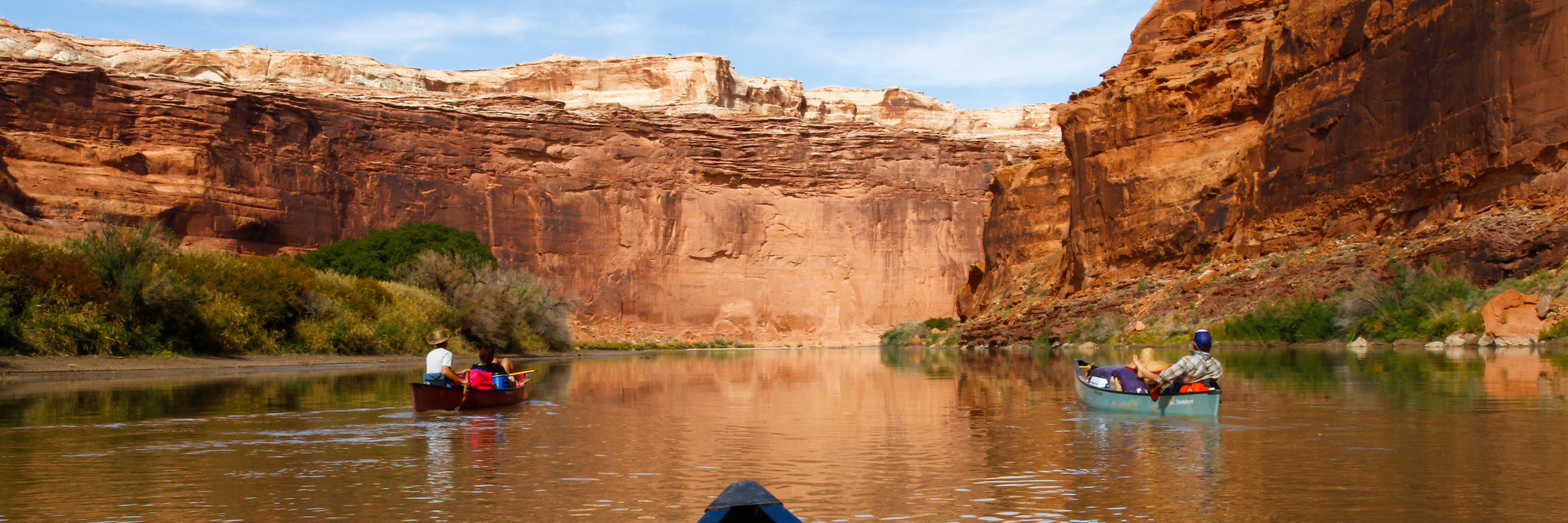 Two canoes full of people float through a red-rock canyon