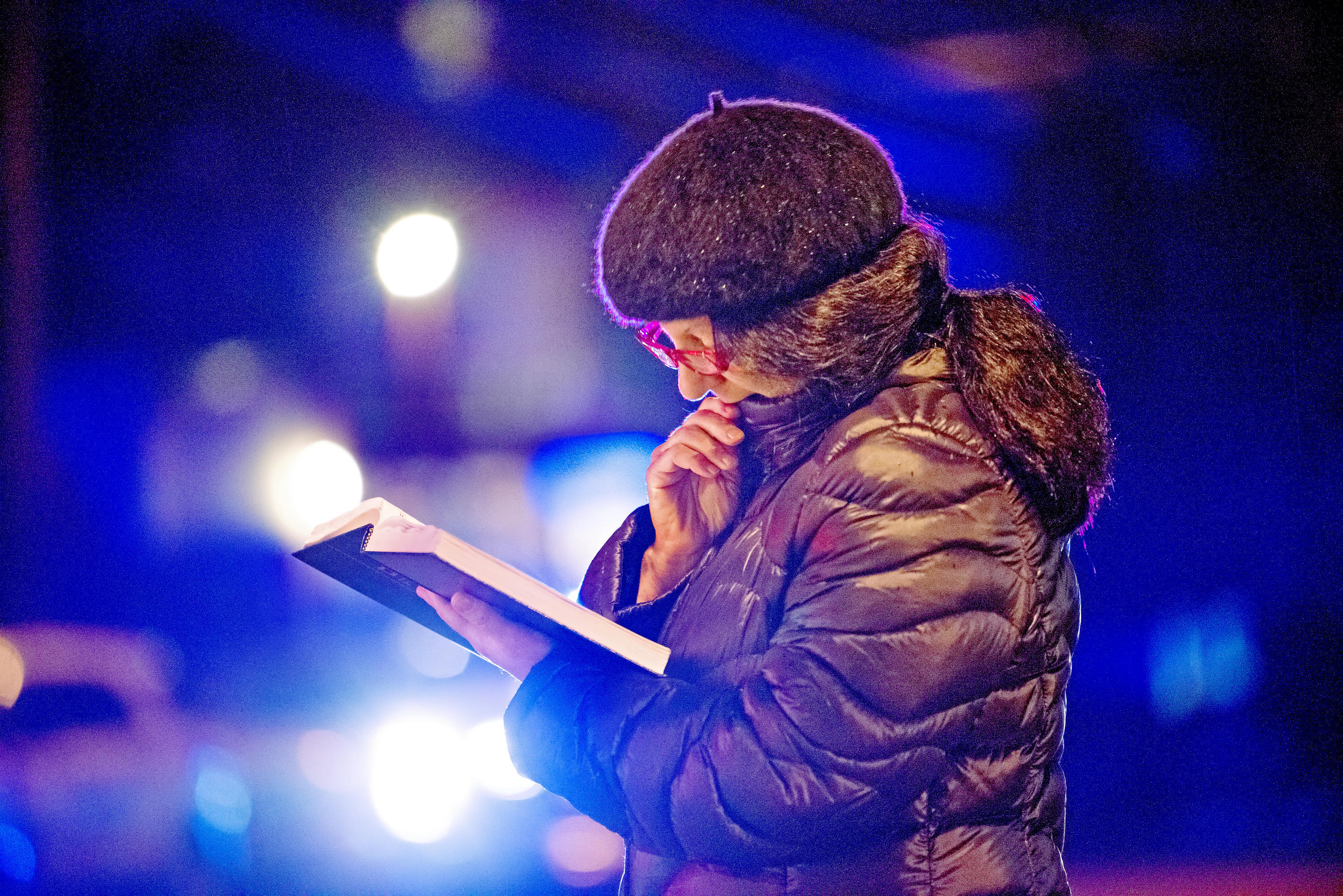 Nancy Clark of Squirrel Hill, reads from the Tehillim, as police lights flash and rain soaks the pages, yards away from Tree of Life Congregation, on Saturday, Oct. 27, 2018, in the Squirrel Hill section of Pittsburgh. A shooter opened fire at the synagogue, killing multiple people and wounding others in one of the deadliest attacks on Jews in U.S. history.  (Andrew Stein/Pittsburgh Post-Gazette via AP)
            