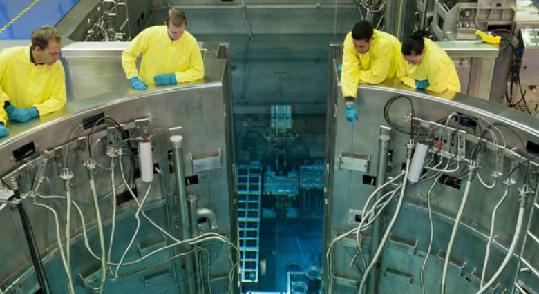 Workers in yellow lab coats on the rim of a reactor looking down into it