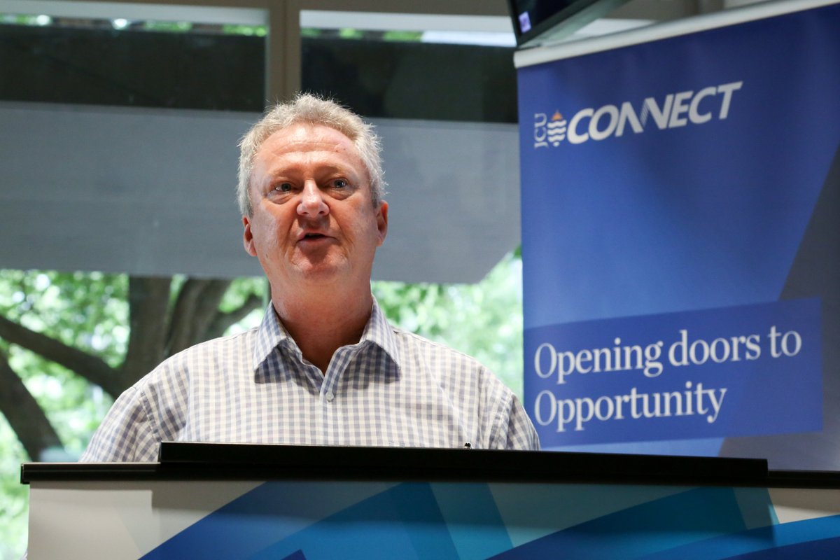 a man speaks at a lectern, a banner behind him say "JCU Connect, opening doors to opportunity"