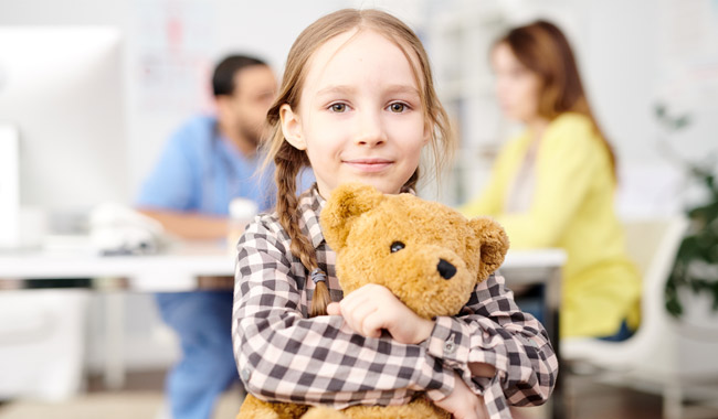 girl holding teddy bear with parents in background