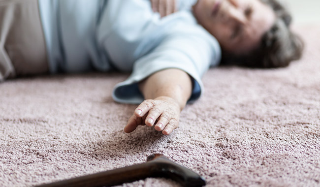 older woman laying on floor reaching for walking cane