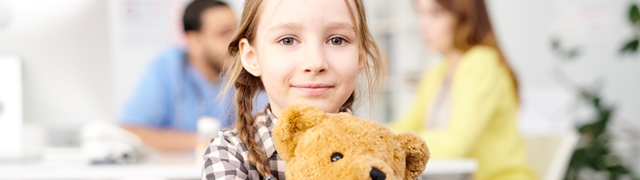Child holding her teddy bear with parent talking to doctor in background