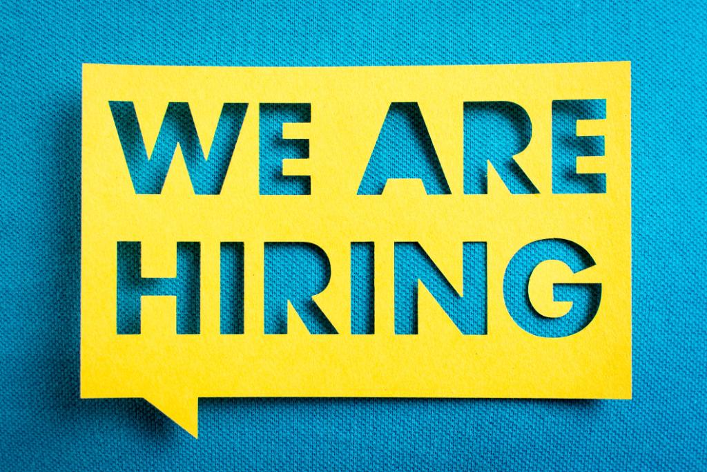 We're Hiring yellow cutout on top of blue jean background.