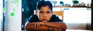 9-year-old Deron sitting at dining room table looking sad