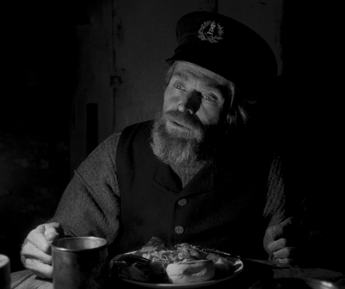 Thomas (Dafoe) speaks over a plate of food and a cup.