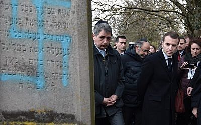 Illustrative: French President Emmanuel Macron looks at a grave vandalized with a swastika during a visit at the Jewish cemetery in Quatzenheim, on February 19, 2019, on the day of nationwide marches against a rise in anti-Semitic attacks. (Frederick Florin/Pool/AFP)