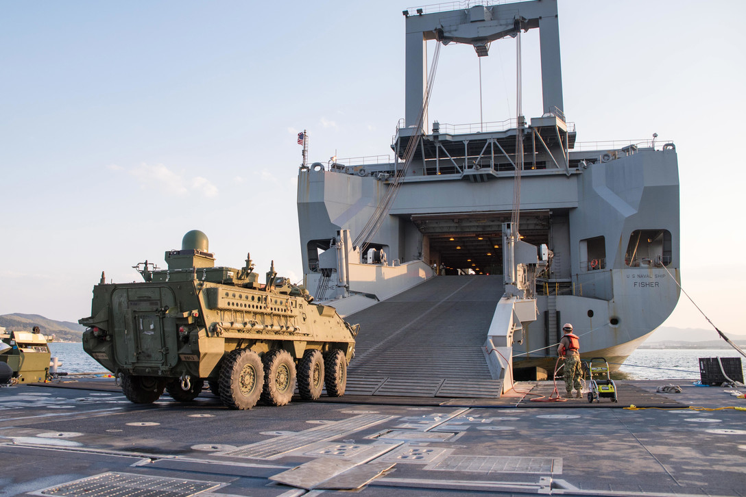 A tactical vehicle drives onto a ship's ramp.