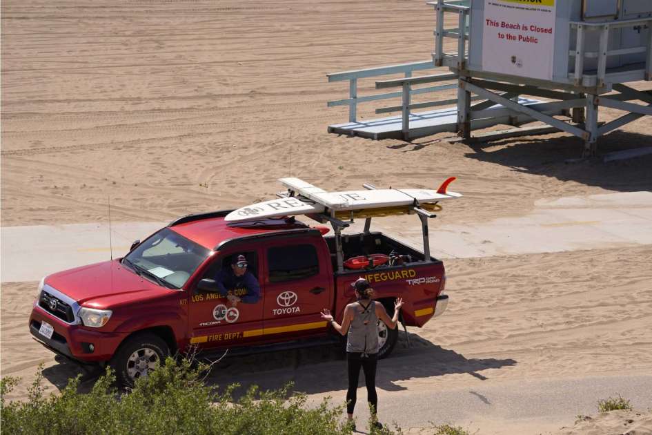 A Los Angeles County Lifeguard speaks to a jogger that was running on closed Playa Del Rey Beach, Friday, April 3, 2020, in Los Angeles. The new coronavirus causes mild or moderate symptoms for most people, but for some, especially older adults and people with existing health problems, it can cause more severe illness or death.