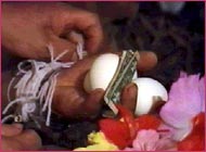 strings tied around wrists of hand holding eggs and money as part of ritual